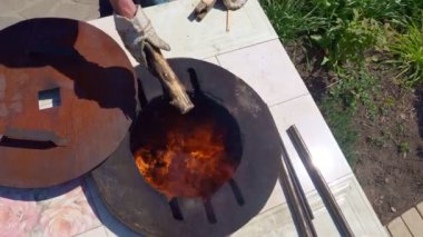 Bir adam yerden tandir fırınına odun atar.