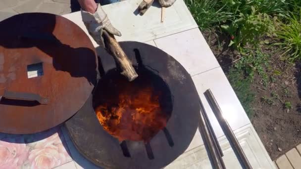 Een man gooit hout in bovengrondse tandir oven — Stockvideo