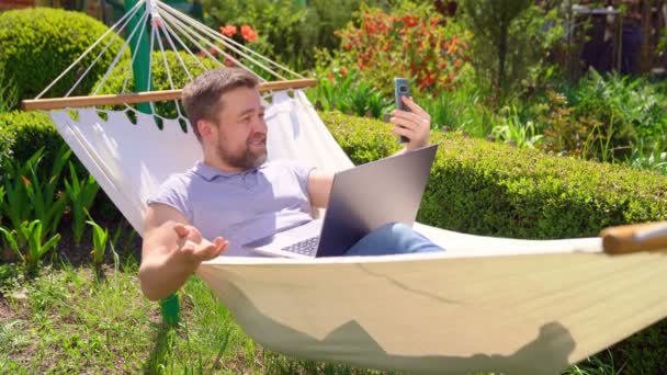 Man ligt in hangmat en werken op de computer — Stockvideo