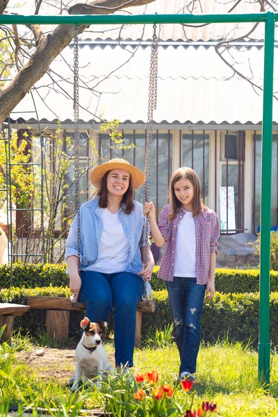 mom and daughter with dog on swing in garden