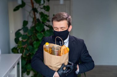 Siyah maskeli işadamının elinde yiyecek paketi var.