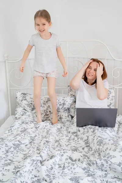 Niña interfiere mamá freelancer trabajo en la cama — Foto de Stock