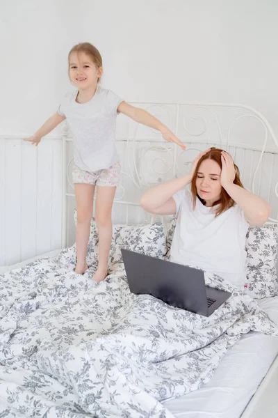 Hija interfiere mamá freelancer para trabajar en la cama . — Foto de Stock