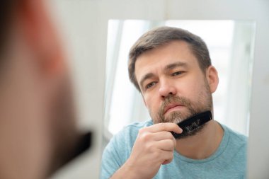 Adam aynaya bakarak saçlarını ve sakallarını tarıyor..