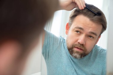 Adam aynaya bakarak saçlarını ve sakallarını tarıyor..