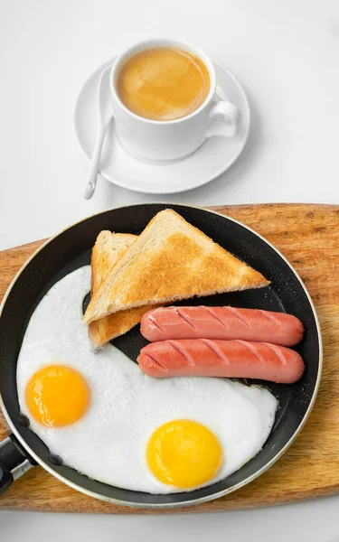 Πρωινό. λουκάνικα, αυγά, ψωμί σε τηγάνι. καφές — Φωτογραφία Αρχείου