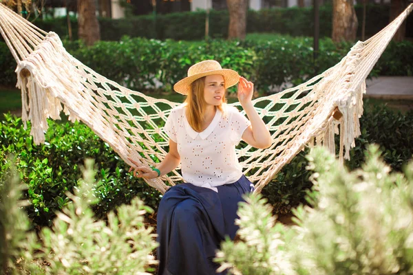 woman in hat and blue skirt sit on hammock in Park