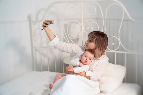 Mamá con el bebé en la cama tomando selfies — Foto de Stock