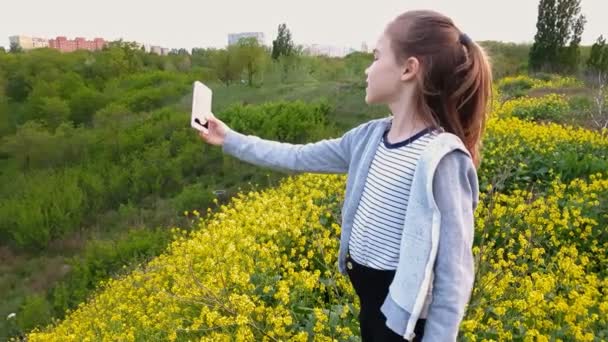 Kız sarı çiçeklerle tepede durarak selfie çekiyor. Doğa yürüyüşü. çocuklar için aktif yaşam biçimi. — Stok video