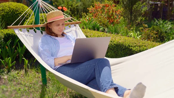 Vrouw ligt in hangmat en werken op de computer Stockfoto