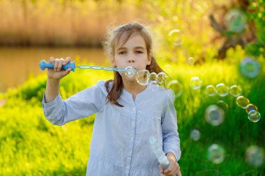 Küçük kız piknikte sabun köpüğü şişiriyor.