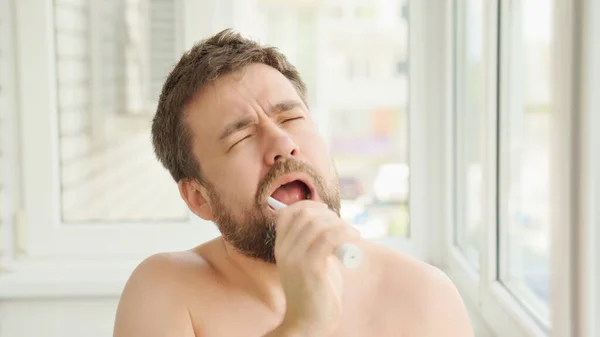 sleepy man cleans teeth electric toothbrush