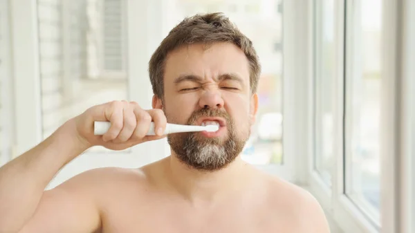 眠い男歯をきれいにする電動歯ブラシ — ストック写真