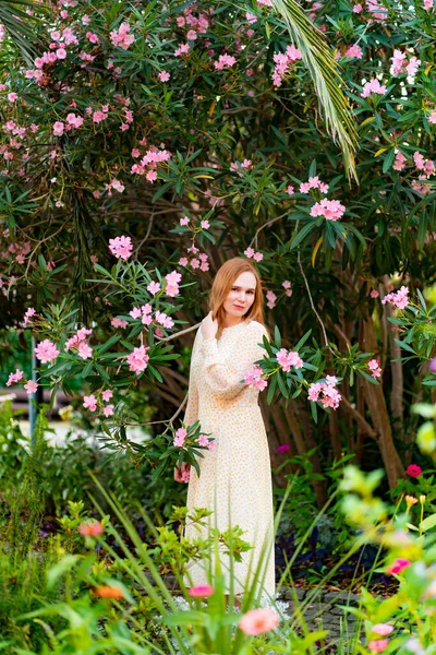 Una mujer en un vestido blanco entre rosales florecientes — Foto de Stock