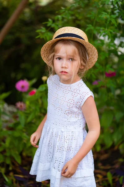 Droevig klein meisje met hoed, witte jurk tussen groen — Stockfoto