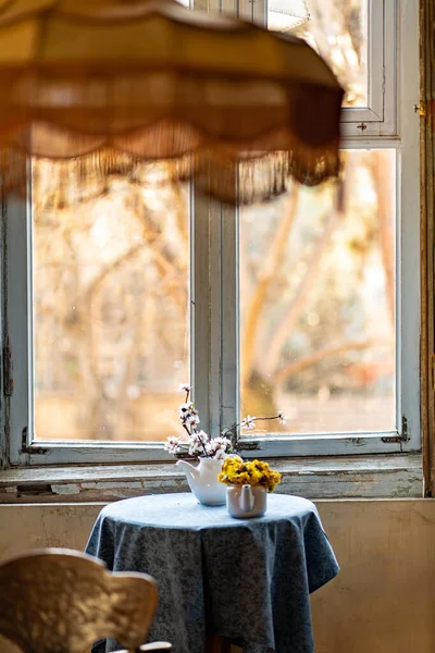 Czajniki z białymi gałęziami kwitnącego drzewa i mniszki lekarskie na stole przez okno — Zdjęcie stockowe