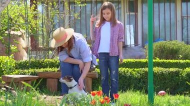 Anne ve kızı köpekle bahçede salıncakta sallanıyor.