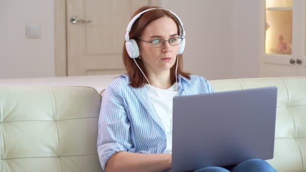 Mujer trabaja en una computadora, tecleando auriculares — Vídeo de stock