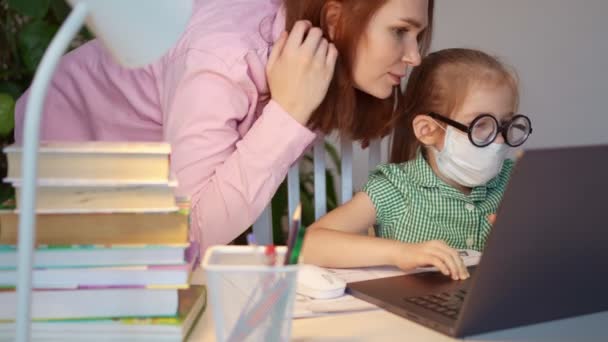 Mamma och dotter med glasögon och medicinsk mask gör lektioner, distansundervisning — Stockvideo