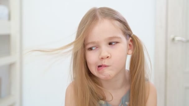 Menina com longo cabelo loiro sopra o cabelo fora de seu rosto e faz rostos — Vídeo de Stock