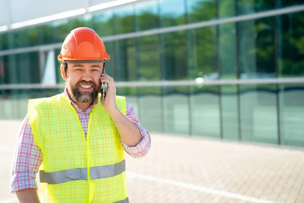 A man supervisor in a construction helmet answers phone call