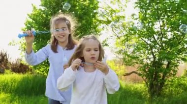İki küçük kız kardeş piknikte sabun köpüğü şişiriyor.