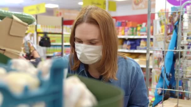 Comprador pelirroja mujer con una máscara protectora selecciona productos — Vídeos de Stock
