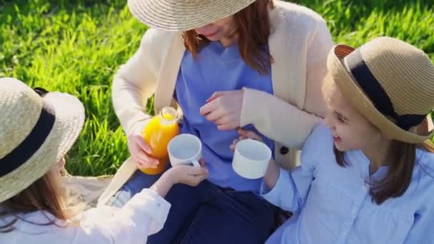 Mom with daughters in hats at picnic on lawn. — Stock Video