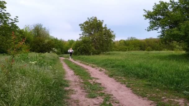 Una adolescente corre por un sendero en un campo . — Vídeo de stock