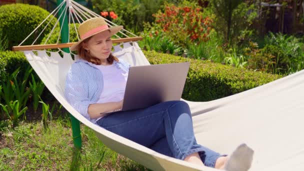 Vrouw in hoed ligt in hangmat, neemt telefoon op — Stockvideo