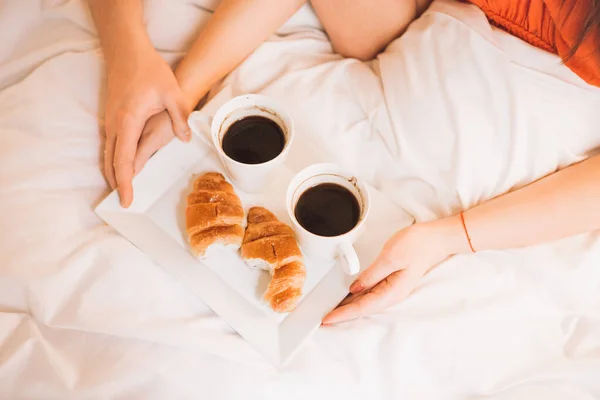 Χέρια αγαπώντας ζευγάρι έχοντας πρωινό στο κρεβάτι με καφέ και κρουασάν. — Φωτογραφία Αρχείου