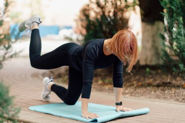 Spor kıyafetli kız sporcu Park 'taki Mat' te bacak kaldırma hareketi yapıyor.. 