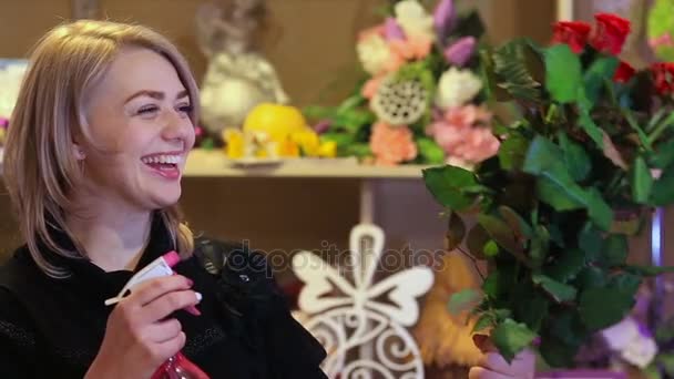 Молода іспаномовна жінка працює флористом у квітковому магазині і дивиться на камеру, посміхається з букетом на столі — стокове відео