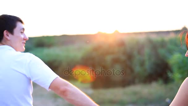 Coppia che cammina in un campo e si tiene per mano al tramonto . — Video Stock