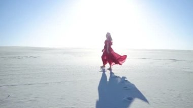 Gündoğumu sırasında bir kumul üzerinde yürüyen bir kadın