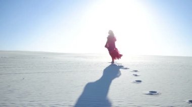 Gündoğumu sırasında bir kumul üzerinde yürüyen bir kadın