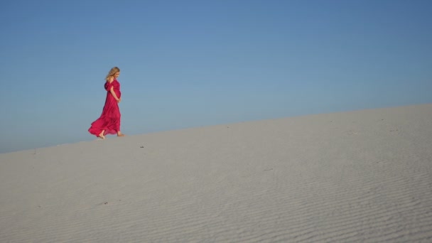 Blond meisje lopen in de wind naar de camera op een duin — Stockvideo