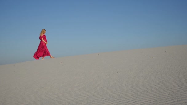 Chica rubia caminando en el viento hacia la cámara en una duna — Vídeos de Stock