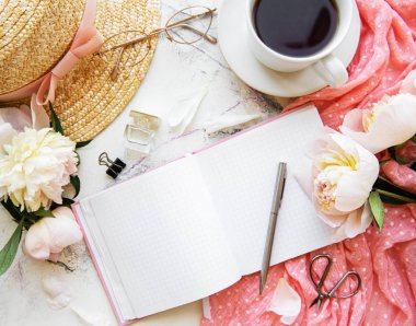 Flat lay blogger or freelancer workspace with a  notebook, pink peonies on a white marble table