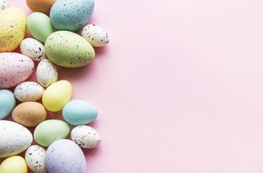 Paskalya tatili geçmişi. Pastel pembe arka planda renkli Paskalya yumurtaları. Düz yatış, üst görünüm.