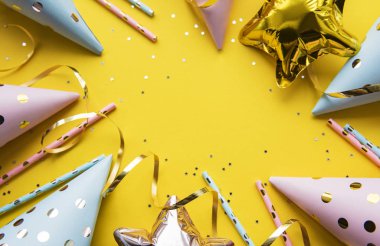Happy birthday or party background.  Flat Lay wtih birthday hats, confetti and ribbons on yellow background. Top View.  Copy space.