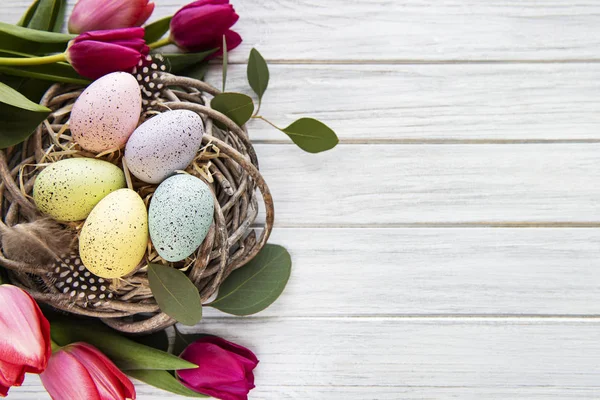 Påskens Bakgrunn Med Fargerike Egg Rede Rosa Tulipaner Hvit Trebakgrunn – stockfoto