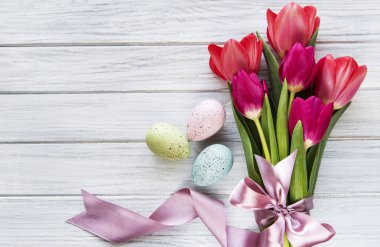 Beyaz ahşap arka planda bahar laleleri ve Paskalya yumurtaları