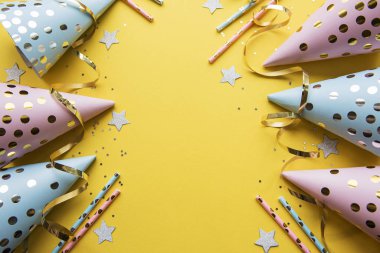 Happy birthday or party background.  Flat Lay wtih birthday hats, confetti and ribbons on yellow background. Top View.  Copy space.