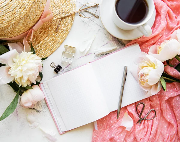 Flat lay blogger or freelancer workspace with a  notebook, pink peonies on a white marble table