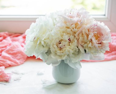 Pencerede vazoda şakayık çiçekleri olan bir masada hasır şapka.