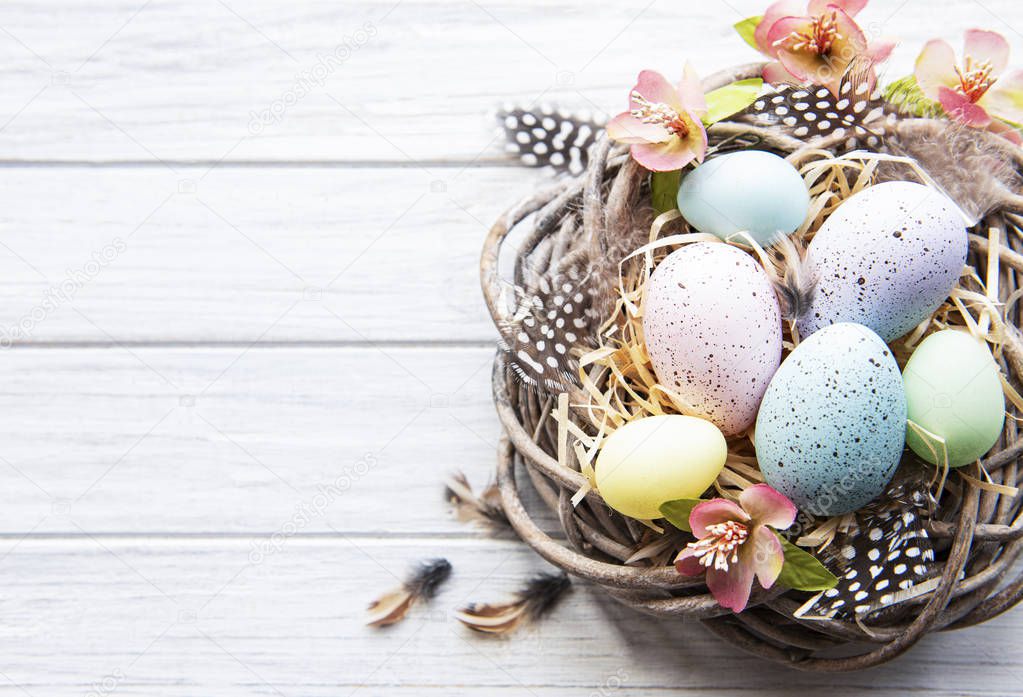 Easter background with colorful eggs in nest  on a white wooden background. Top view with copy space
