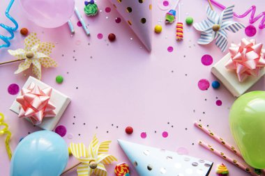 Pembe pastel arka planda pano ve renkli dekorasyonlar. Düz yerde, üst tarafta. Doğum günü geçmişi, tatil kavramı.