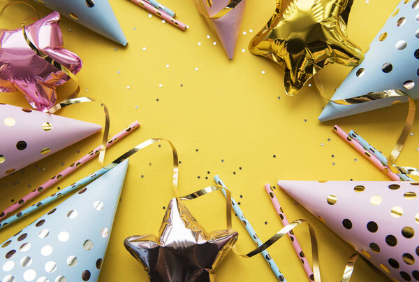 Happy birthday or party background.  Flat Lay wtih birthday hats, confetti and ribbons on yellow background. Top View.  Copy space.