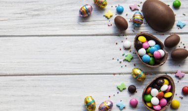 Beyaz ahşap arka planda renkli ve çikolatalı yumurtaları olan Paskalya kompozisyonu, yazı için boşluk. Üst manzara, düz uzanma. 